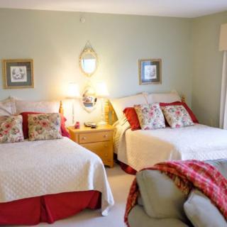 A cozy bedroom featuring two neatly made beds with decorative pillows and a shared nightstand between them, illuminated by warm lamps against a backdrop of soft wall art.