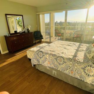 A sunlit bedroom with a large bed, dresser, and a view from the balcony.
