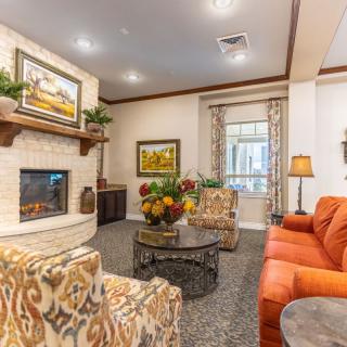 A cozy living room with a sofa, armchairs, and a fireplace, featuring elegant decor and paintings.
