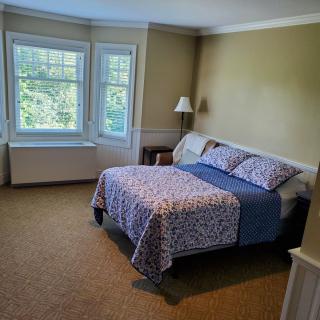 A cozy bedroom with a bed, large windows, and soft lighting.