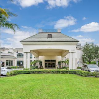 A modern hotel entrance surrounded by lush greenery and a clear blue sky.