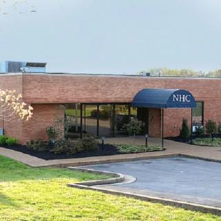 A brick office building with an entrance featuring a blue awning and surrounding landscaping.