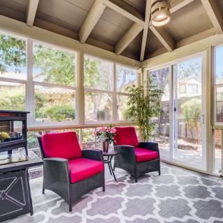 A cozy sunroom featuring two black chairs with red cushions, surrounded by large windows and adorned with an indoor plant.