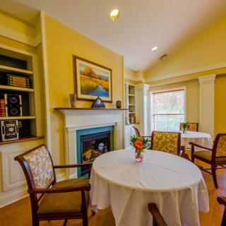 A cozy dining area with a table and chairs, featuring a fireplace and decorative shelves.