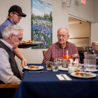 Elderly men being served a meal in a restaurant setting.
