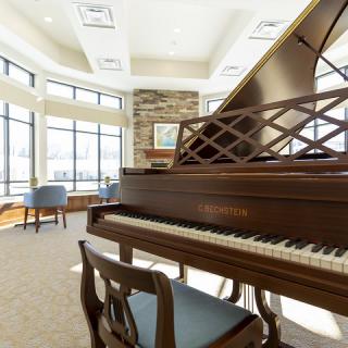 A spacious music room featuring a grand piano, with abundant natural light streaming through large windows.