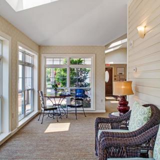 A bright sunroom with large windows, featuring comfortable seating and a dining area.