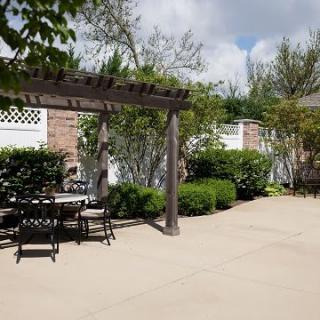 A sunny patio area featuring a pergola with outdoor furniture and lush garden surroundings.