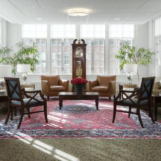 A cozy living room with armchairs, a grandfather clock, and large windows.
