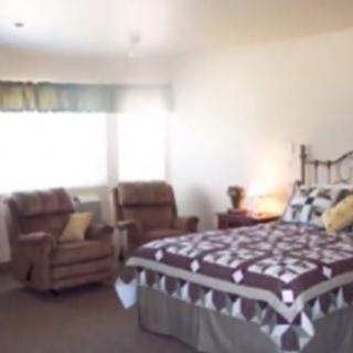 A cozy bedroom with a bed, two chairs, and a window allowing natural light.