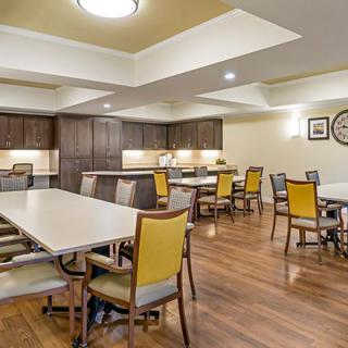 A modern dining area with multiple tables and chairs, featuring a kitchen in the background.