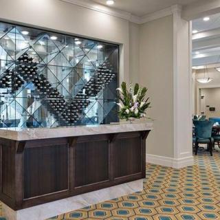 A modern and elegant hotel lobby featuring a reception desk with a decorative wine rack and floral arrangement.