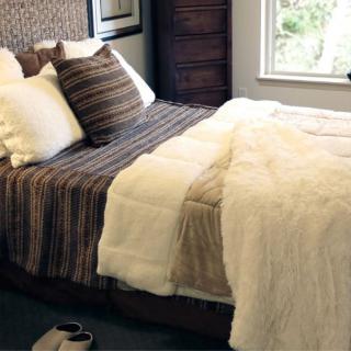 A cozy bedroom featuring a neatly made bed with striped and fluffy pillows, a soft blanket, and a window view.