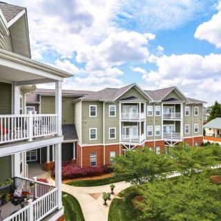 A view of a residential apartment complex with well-maintained landscaping and a bright blue sky.