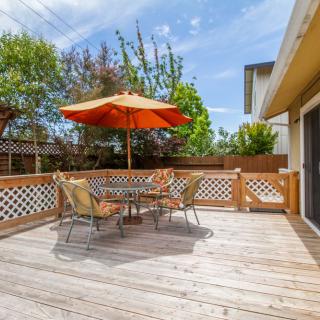 A sunny outdoor patio with a table and chairs, featuring an orange umbrella.