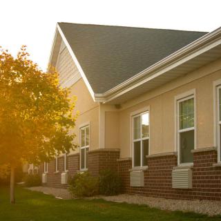 A sunlit exterior view of a building with large windows and a tree nearby.