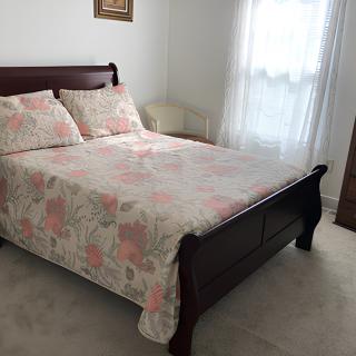 A cozy bedroom featuring a wooden bed with floral bedding and a window with sheer curtains.