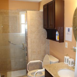 A modern bathroom featuring a glass-enclosed shower, toilet, sink with mirror, and storage cabinet.