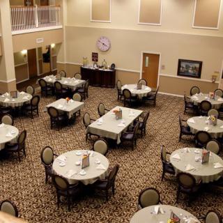 An empty dining hall with round tables and chairs arranged neatly on a carpeted floor.