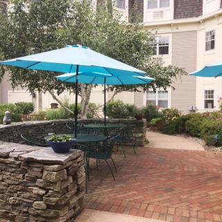 A cozy outdoor patio area with turquoise umbrellas and a stone wall surrounded by greenery.