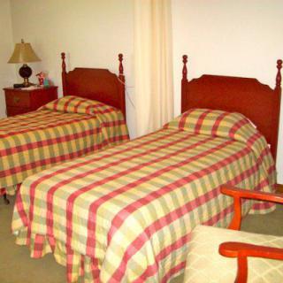 A bedroom with two twin beds, each covered in checkered bedding. A nightstand with a lamp is positioned between the beds.