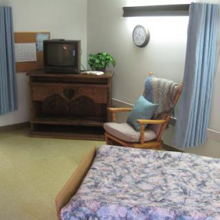 A cozy room featuring a bed, television, and rocking chair with soft blue curtains.