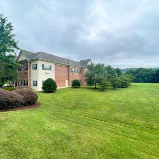 A spacious brick house with a large, well-maintained lawn and trees on a cloudy day.