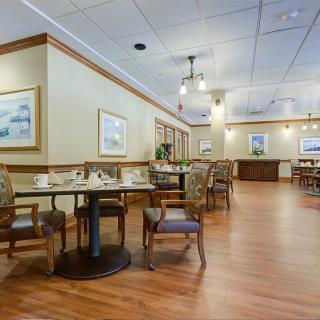 A spacious and elegantly furnished dining area with neatly arranged tables and chairs, featuring wooden flooring and decorated walls.