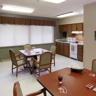 A cozy kitchen and dining area with a wooden table and chairs, featuring white appliances and blinds on the windows.