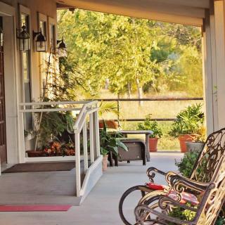 A cozy porch with a bicycle, rocking chair, and potted plants in the sunlight.