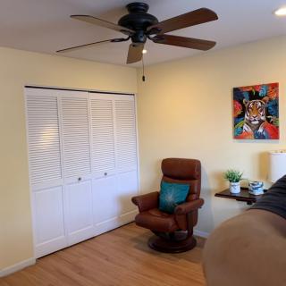 A cozy room featuring a brown chair, a colorful painting, and a ceiling fan.