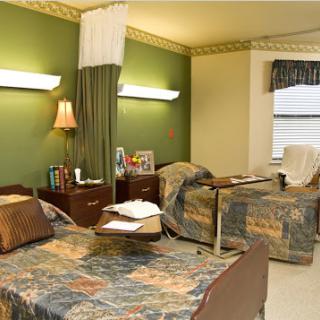 A hospital patient room featuring two beds with decorative covers and a calming green wall.