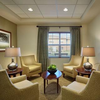 A cozy waiting room with four armchairs, two lamps, and a small central table beneath a window with curtains.