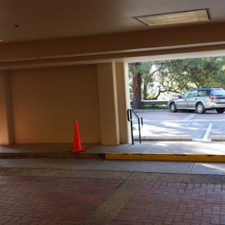 A view of a parking area with a traffic cone and a vehicle parked outside.