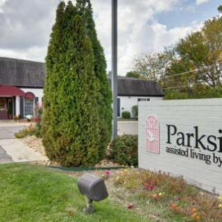 Entrance to an assisted living facility with a sign and landscaped area featuring trees.