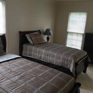 A cozy bedroom featuring two twin beds with matching plaid bedding, a bedside lamp, and windows with blinds.