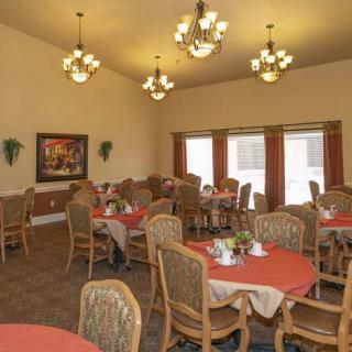 A well-lit dining room featuring several tables and chairs, illuminated by chandeliers.