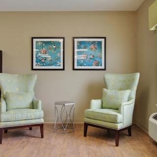A cozy living room with two green armchairs, wall art, and a small round table on a wooden floor.