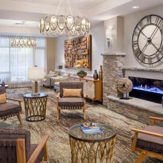 A modern living room with a large wall clock, fireplace, and stylish seating arrangement.