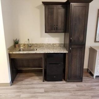 A modern kitchenette with dark wood cabinets, granite countertop, and a small sink.