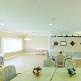 A spacious dining room with tables and chairs, decorated with flowers and well-lit by natural light from large windows.