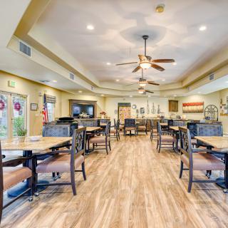 A spacious dining area with neatly arranged tables and chairs, featuring ceiling fans and warm lighting.