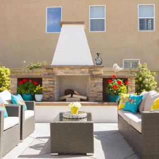 A beautifully decorated outdoor patio with a central fireplace and comfortable seating.
