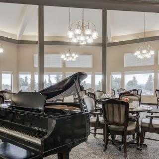 An elegant dining room featuring a grand piano and large windows.