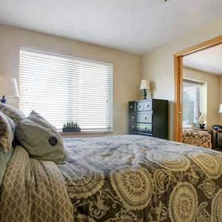 A cozy bedroom with a patterned bedspread, mirror closet doors, and natural light from a window.