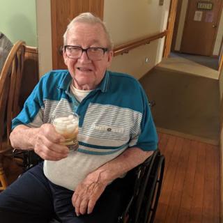 An elderly man enjoying a drink in a care facility.