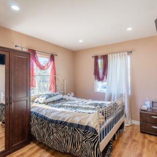 A cozy bedroom with a bed featuring zebra-patterned bedding, a wooden wardrobe, hardwood floors, and curtains on two windows.