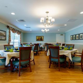 A spacious dining room with neatly arranged tables and chairs, featuring elegant chandeliers and a polished wooden floor.
