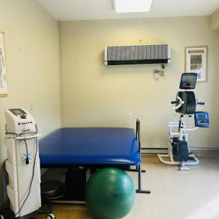 A well-equipped physical therapy room featuring a treatment table, exercise equipment, and a fitness ball.