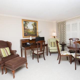 A traditional living room featuring classic wooden furniture, a desk, chairs, an armchair, and framed artwork on the wall.